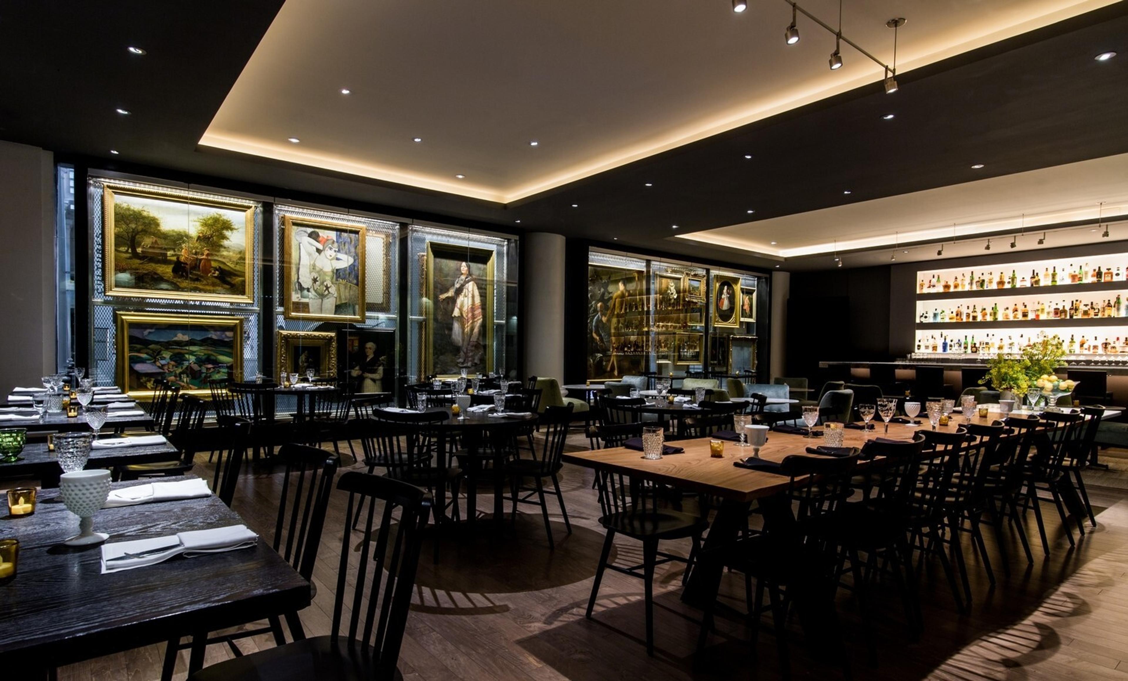 Dimly lit restaurant lined with framed paintings and a backlit bar
