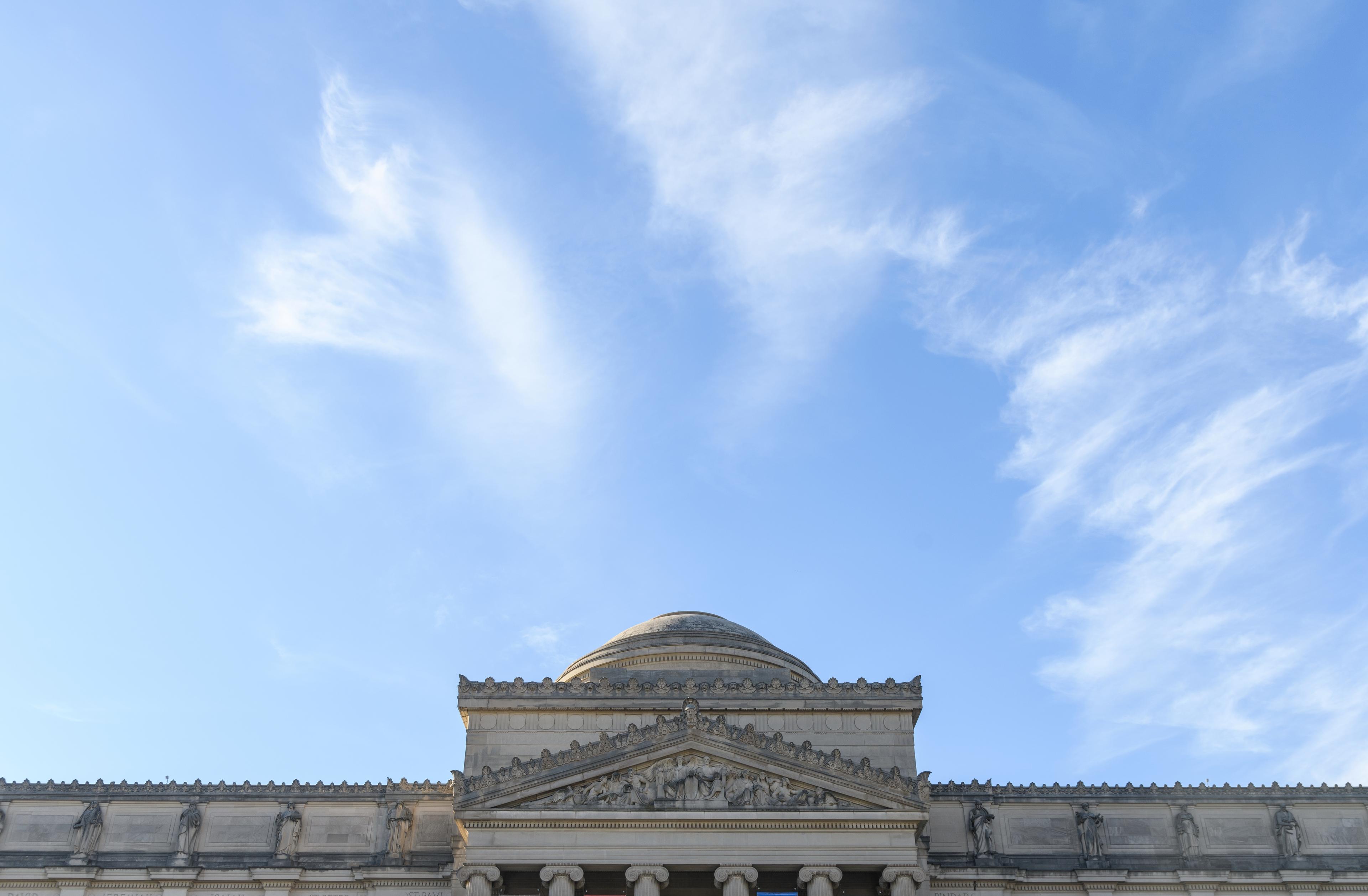 Detail shot at the top of a building facade, featuring relief details, columns, and a domed roof