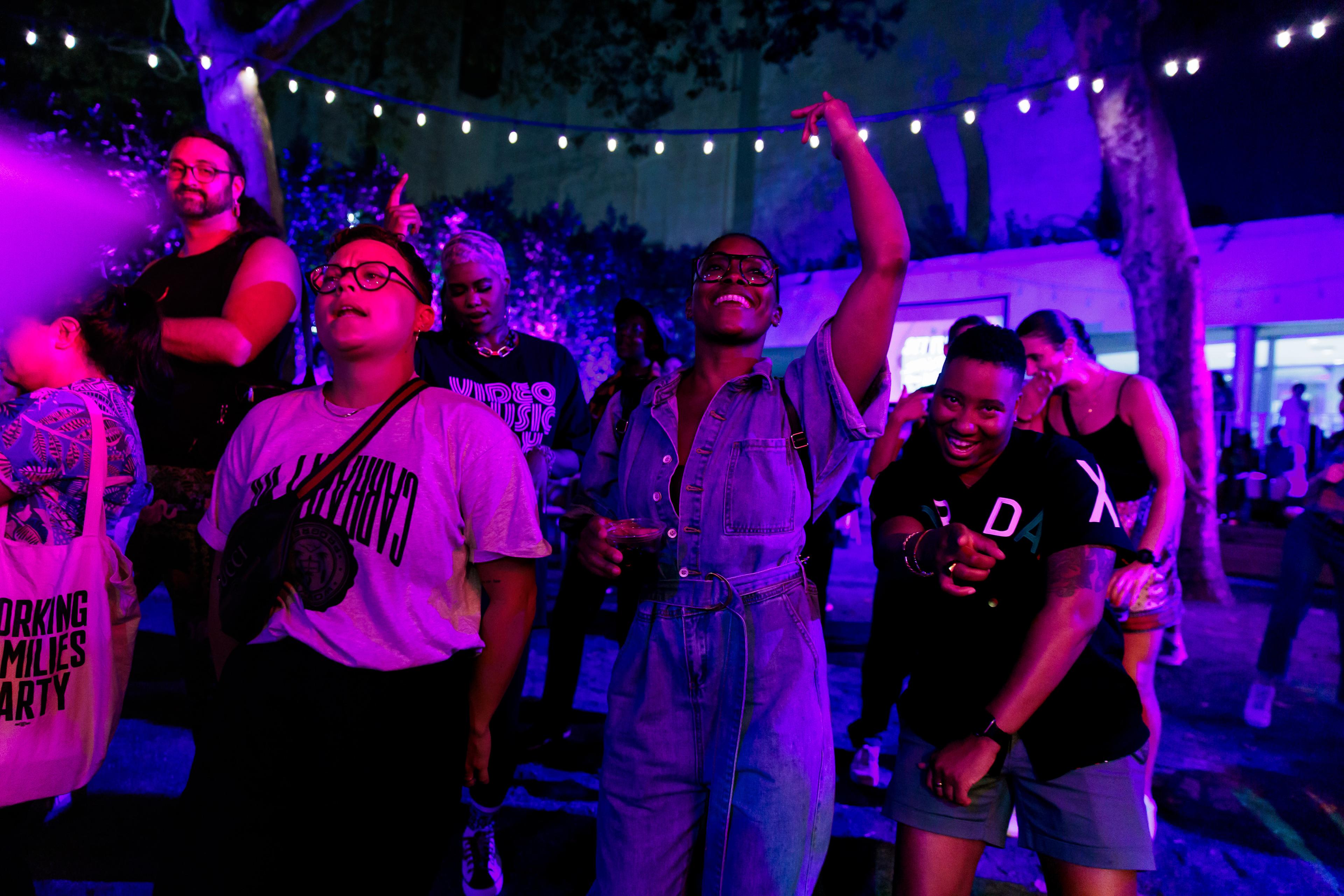 A crowd dances outside bathed in purple light