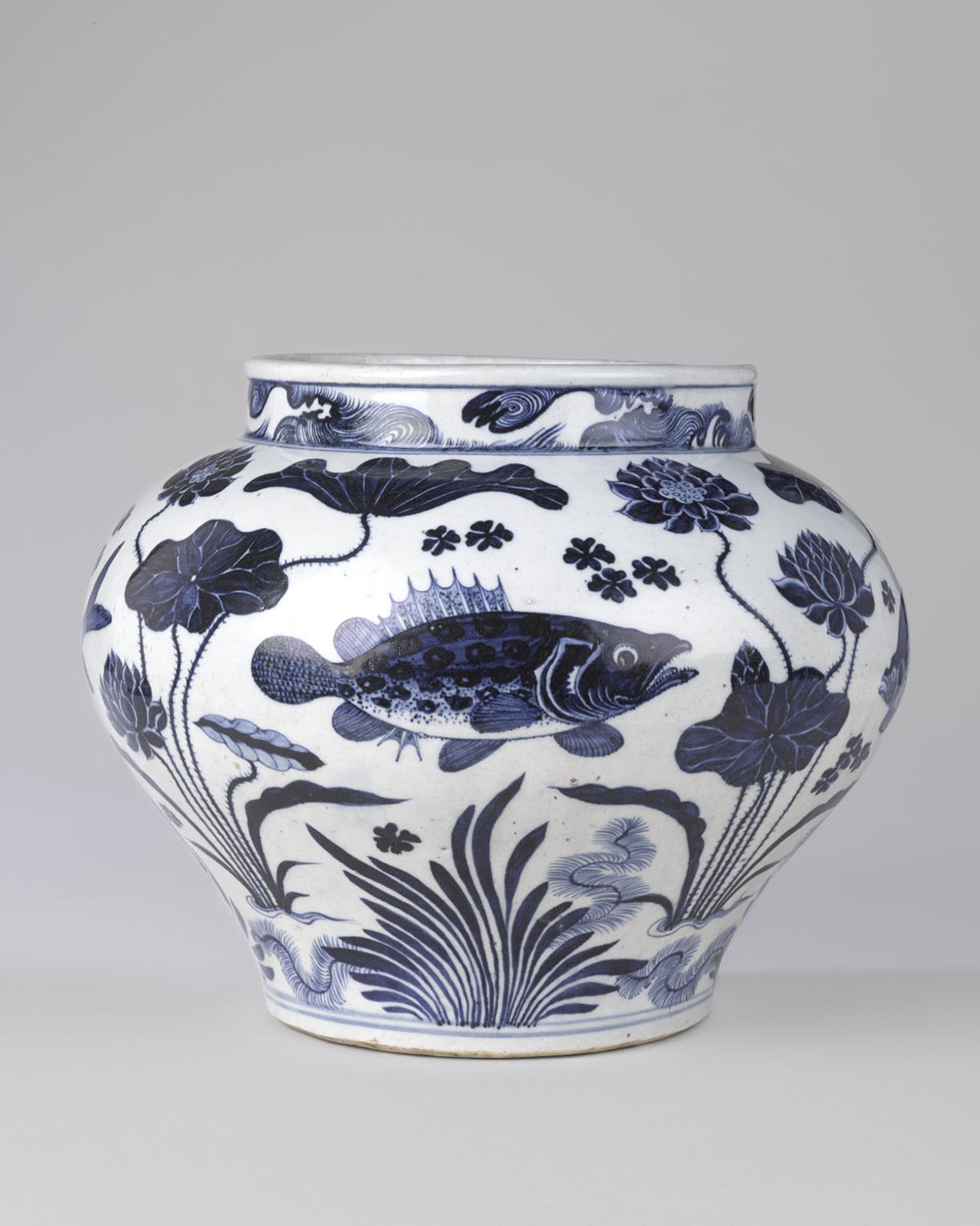 A large porcelain jar with cobalt blue decorations on a white background depicting realistic fish and aquatic plants