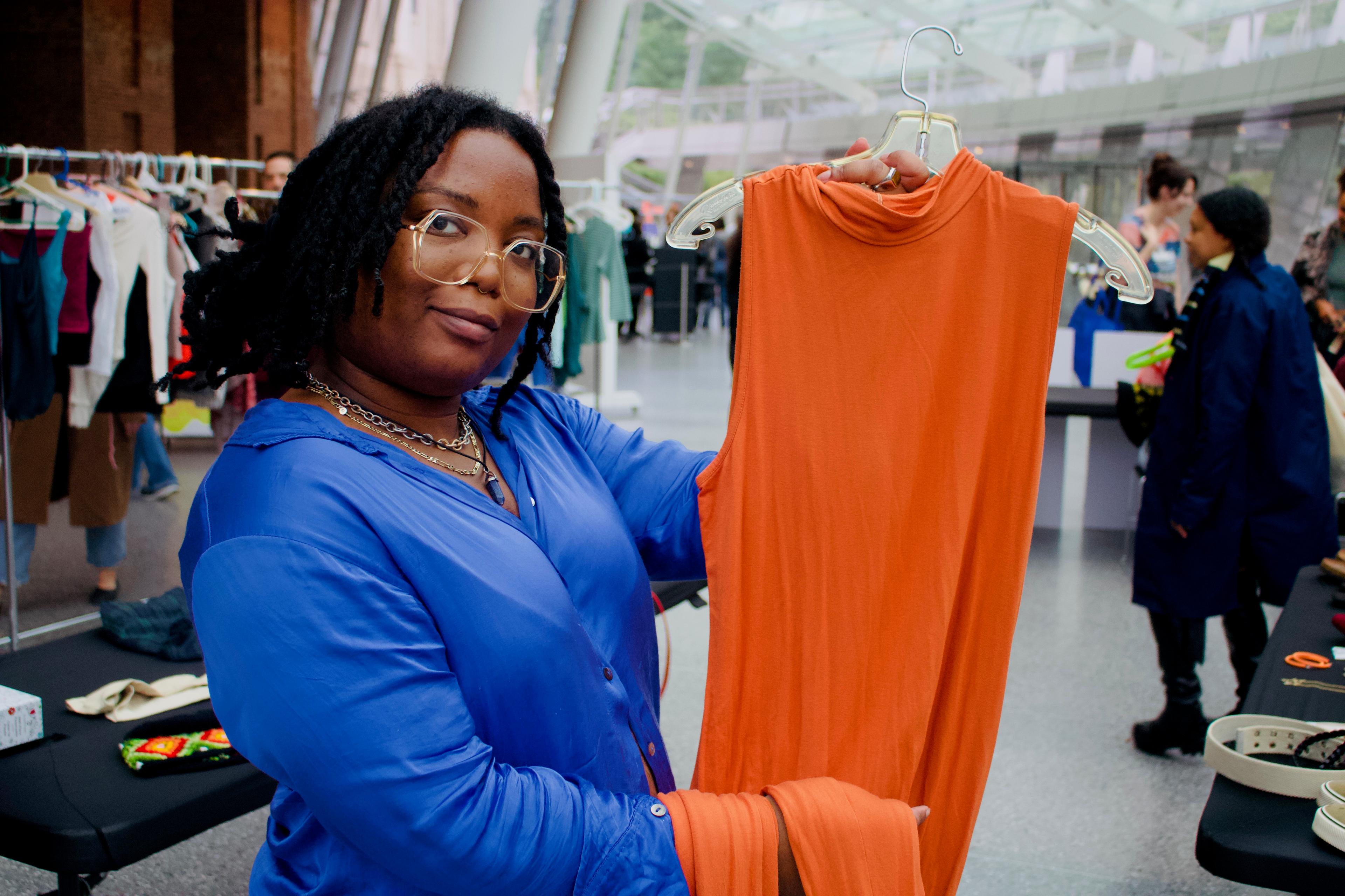 Person in a blue shirt holds an orage dress on a hanger