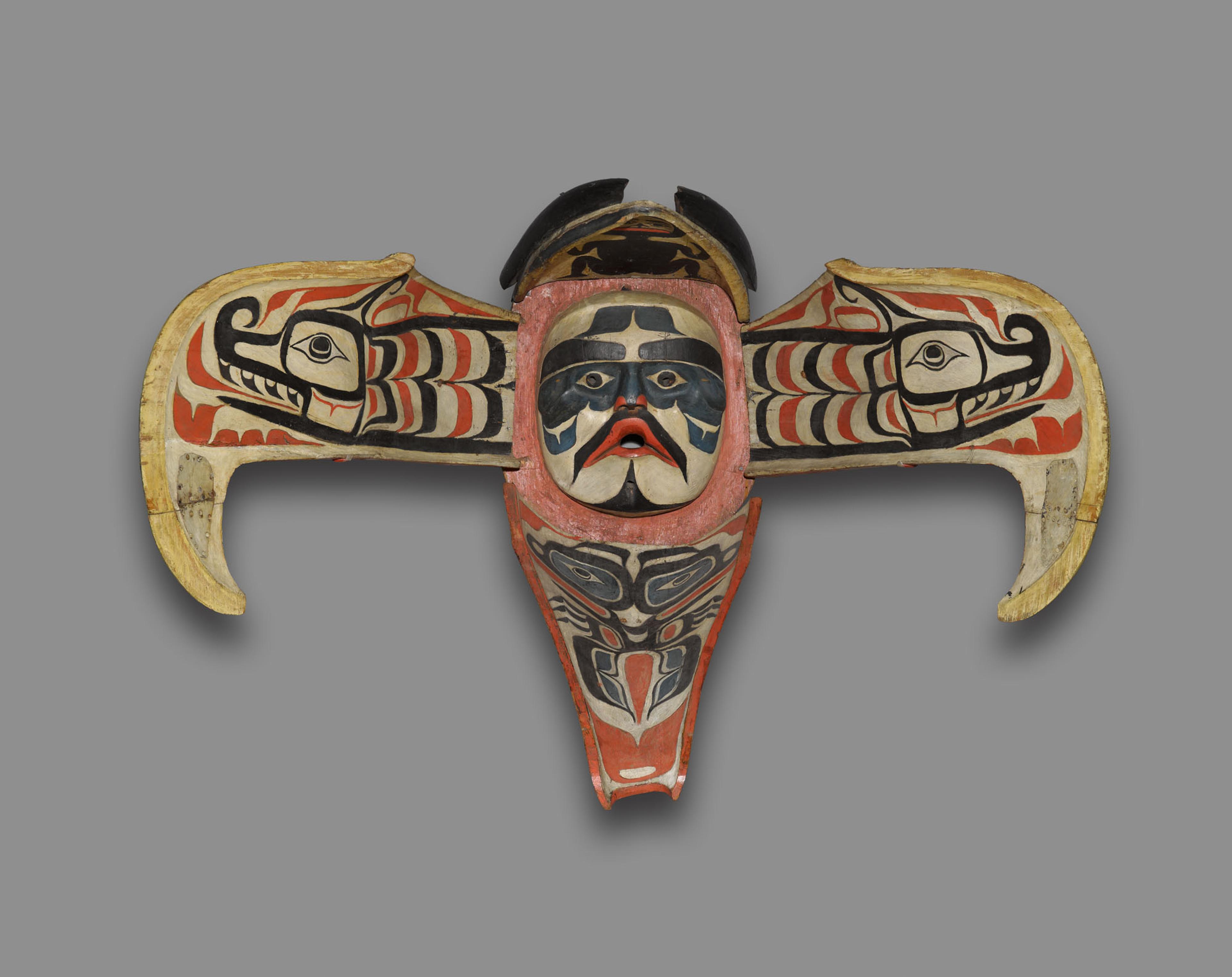 Wooden mask figure with black, white, blue, and red face markings, and out stretched wings showing a serpent like figure