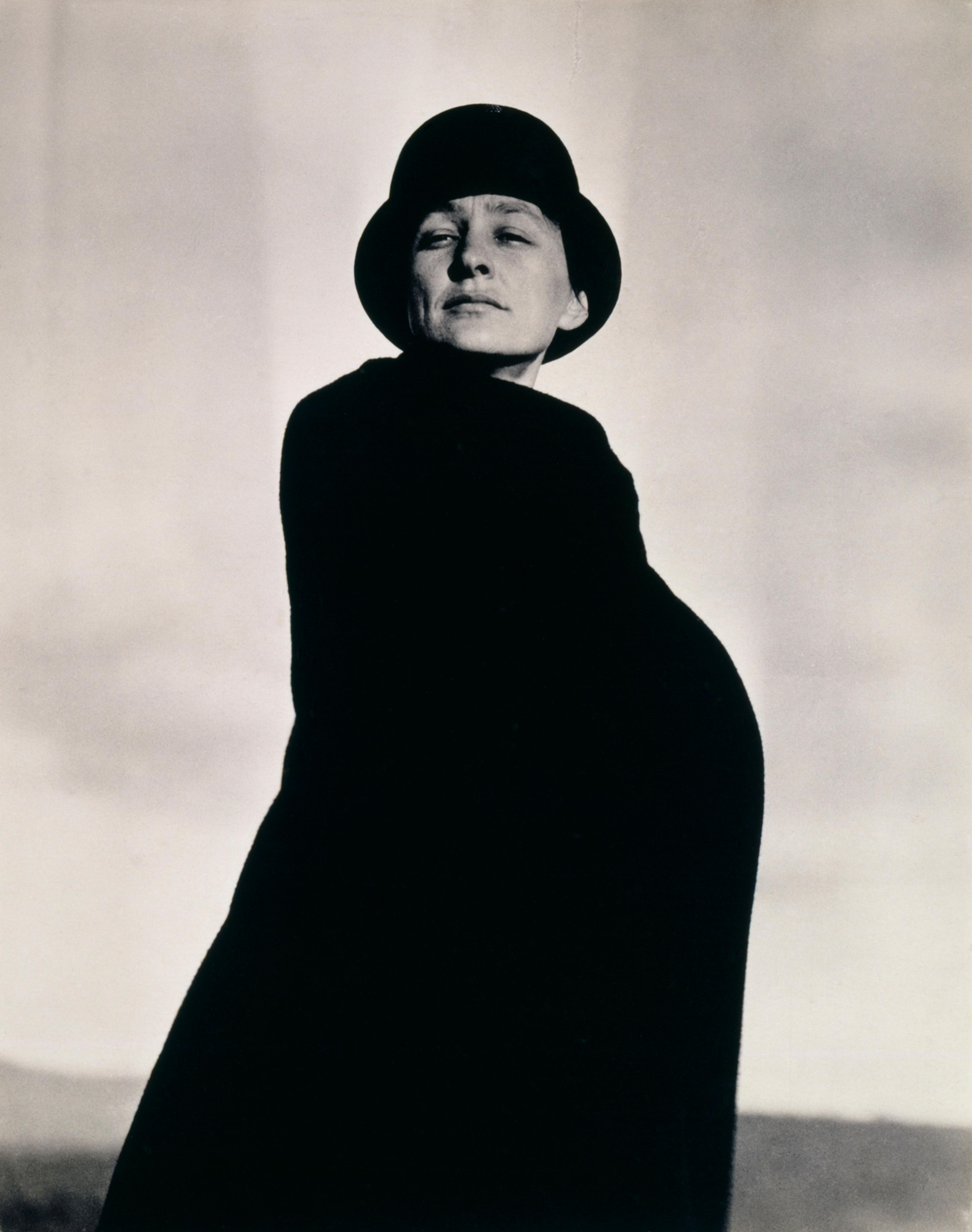 A woman in a dark coat and hat gazes into the distance