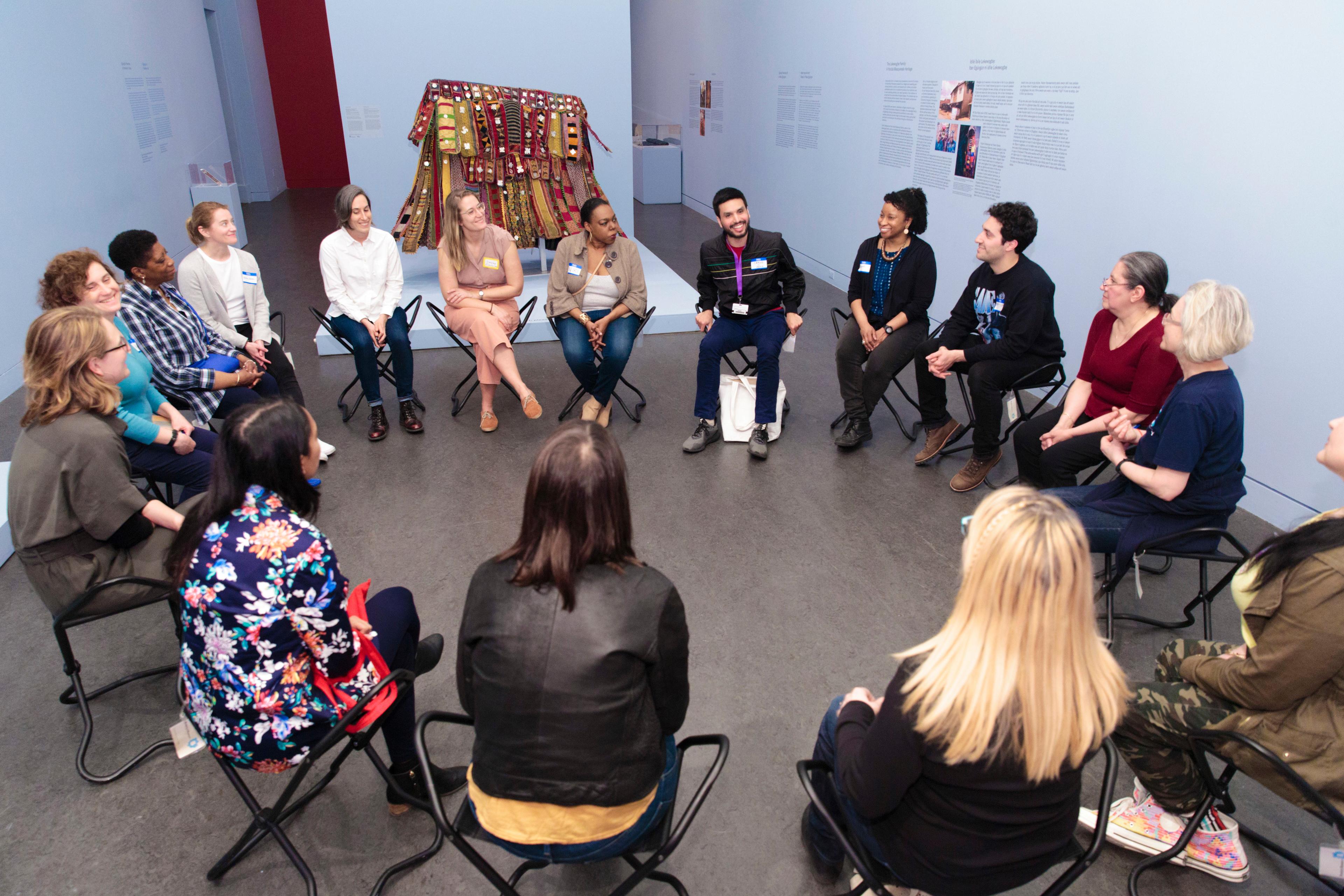 A group of educators sit around in a circle having a discussion in front of an African costume