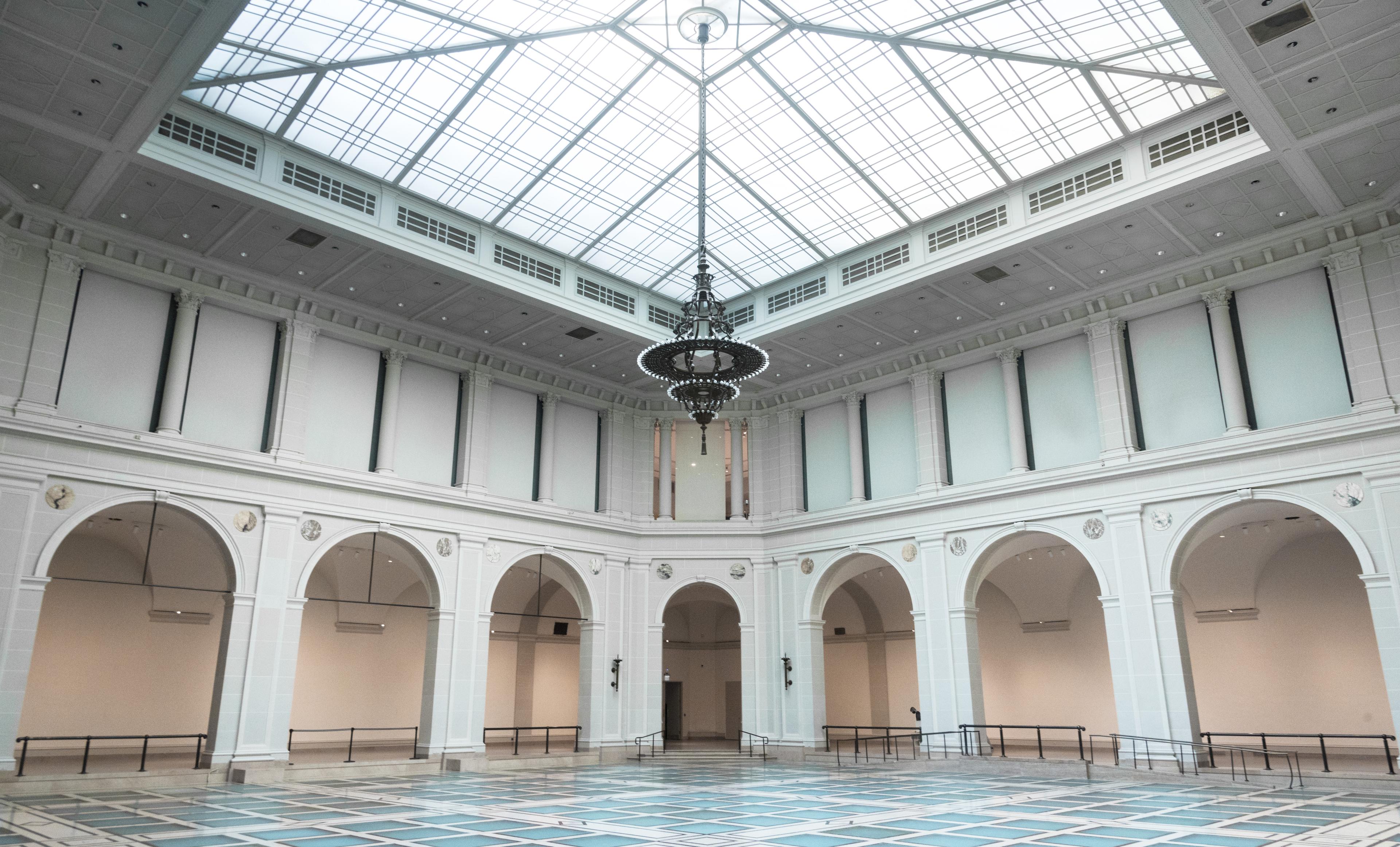 Light-filled, 2-story atrium with large chandelier and glass floor surrounded by arches