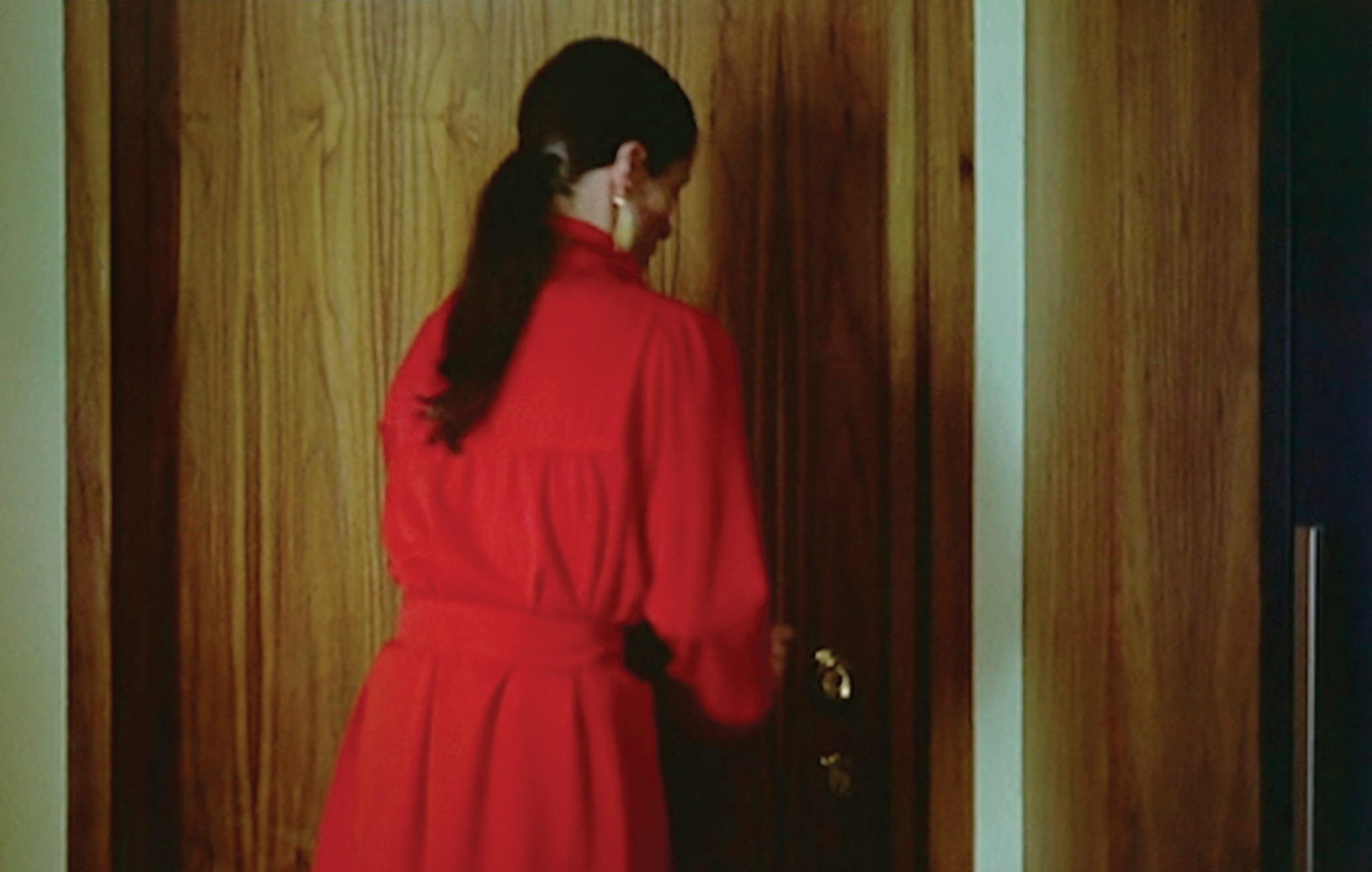 Film still showing a woman in red reaching for a door handle
